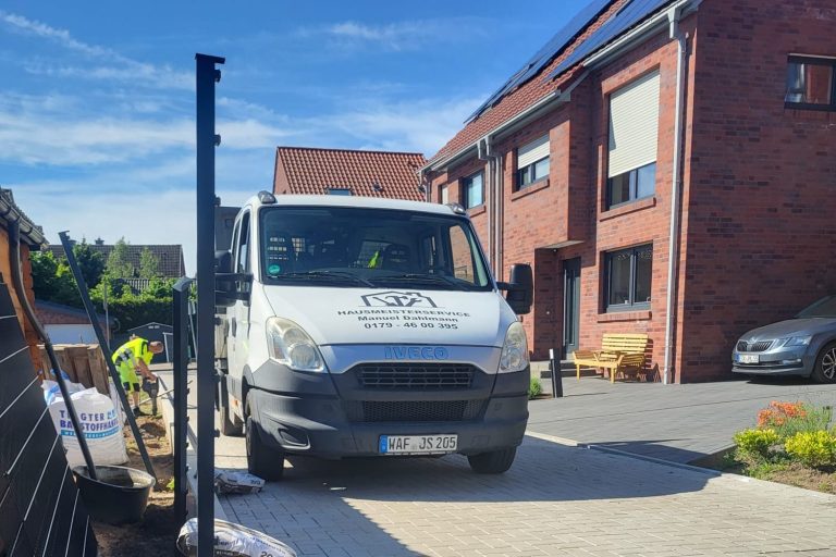 Weißes Lieferfahrzeug steht auf einem gepflasterten Parkplatz vor einem Wohnhaus.